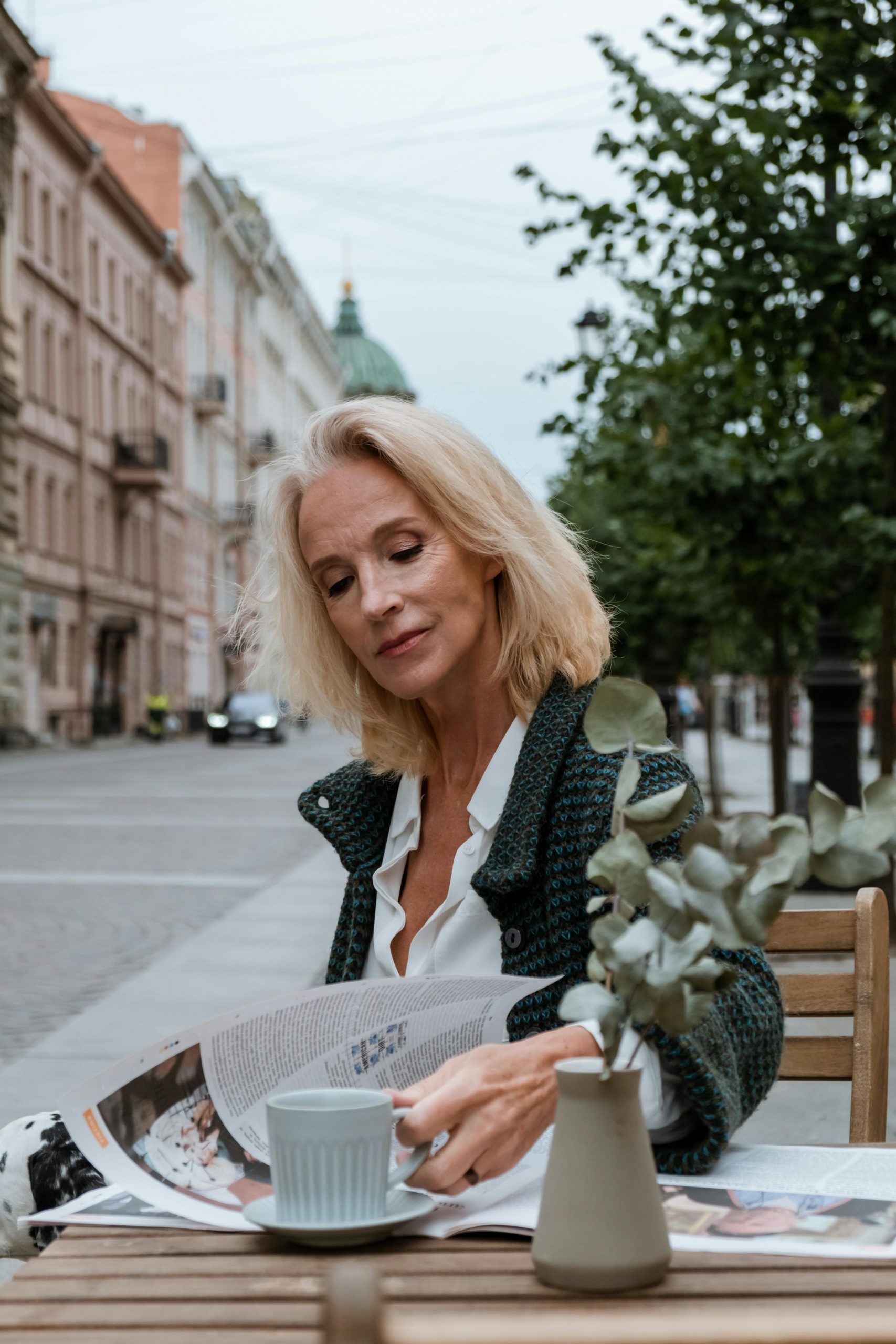 Mature woman reading newspaper at outdoor cafe in city. Summer vibe.
